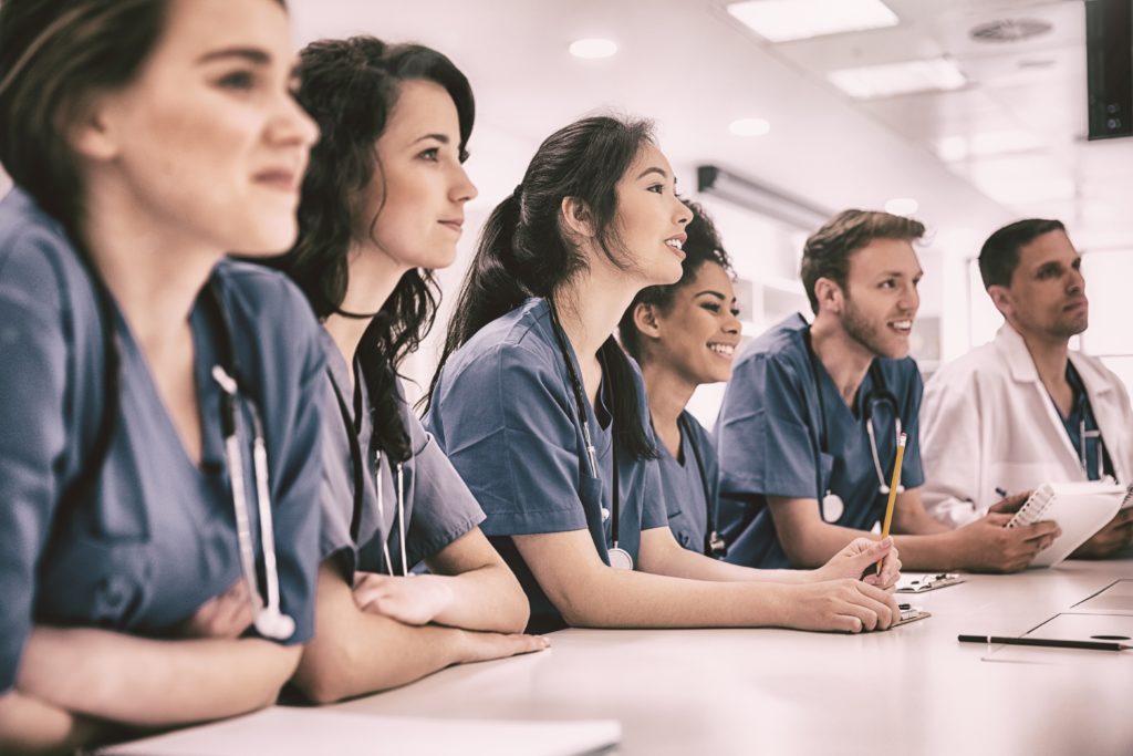 young people in scrubs seated at a table listening.