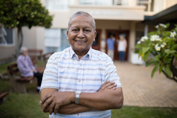 Portrait,Of,Smiling,Senior,Man,Standing,With,Arms,Crossed,Against