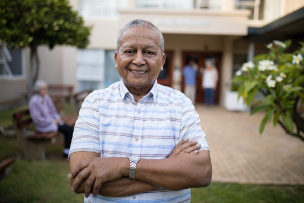 Portrait,Of,Smiling,Senior,Man,Standing,With,Arms,Crossed,Against